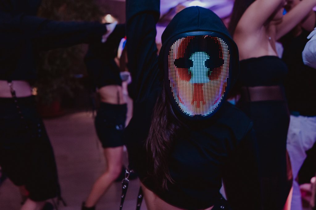 Un performer con la maschera luminosa tra gli ospiti che ballano
