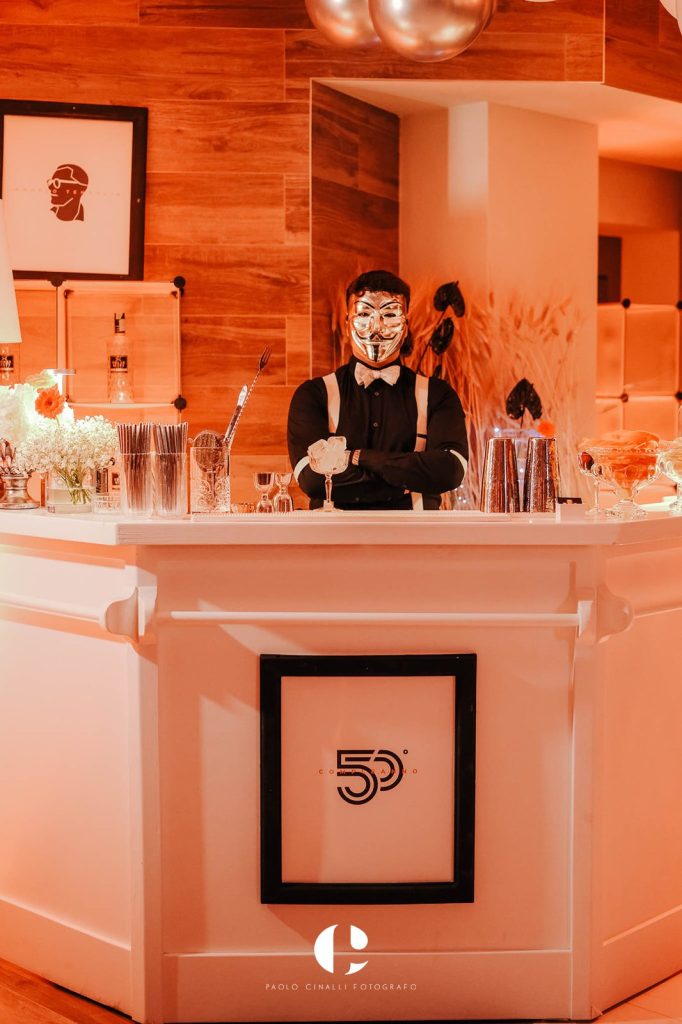 Il bancone del bar con il barman mascherato e il logo dei 50 anni