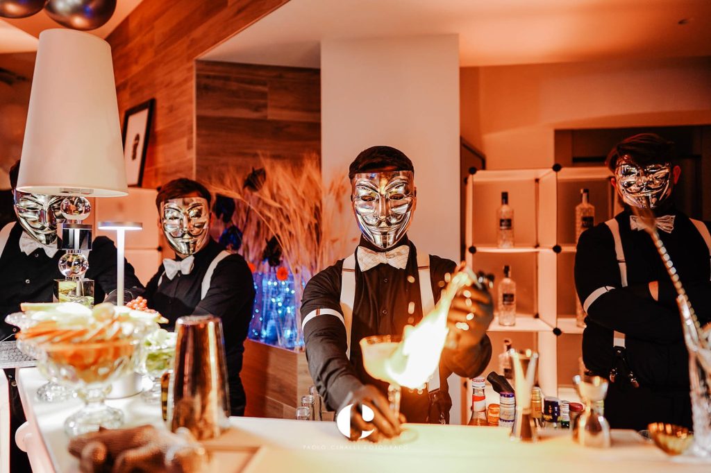 Barman con la maschera argentata preparano cocktail con il fuoco