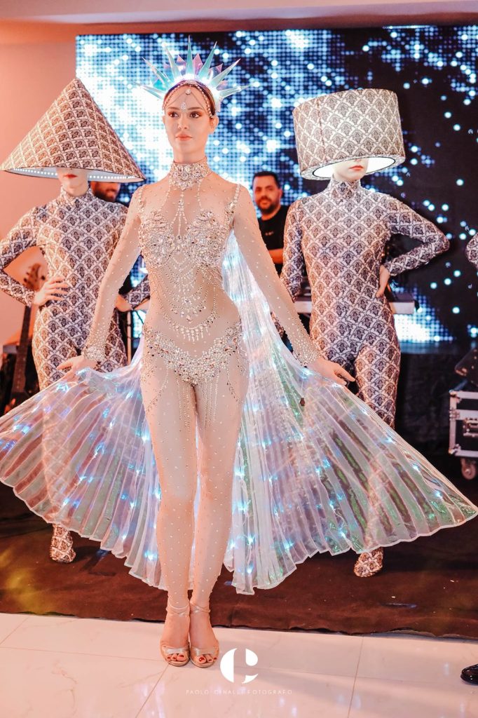 Performer con le ali di luce tra due figure con il cappello a cono