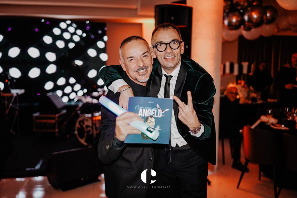Angelo con un amico che mostra il libro “Non sono un angelo”