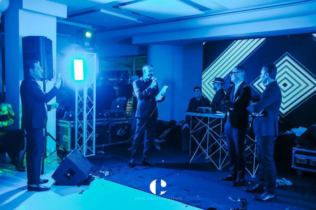 Sul palco, in luce blu, un discorso al microfono