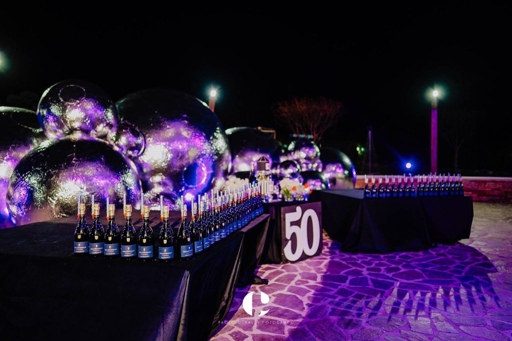 Sfere illuminate di viola in giardino e bottiglie allineate accanto al 50