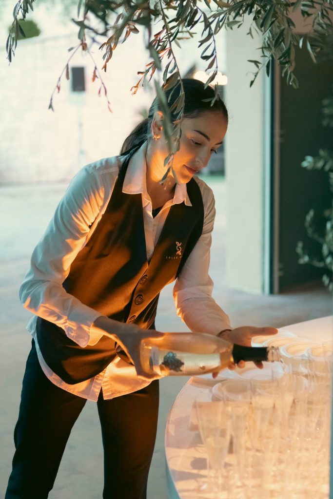 Una hostess serve da bere sotto i rami d'ulivo